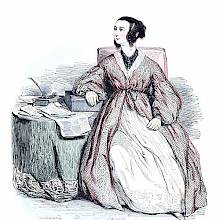 A woman in a dressing gown is sitting at a table covered with papers