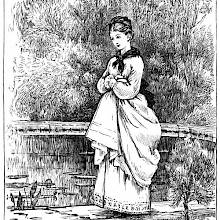 A young woman with a faint smile on her lips walks along a low wall, with trees in the background